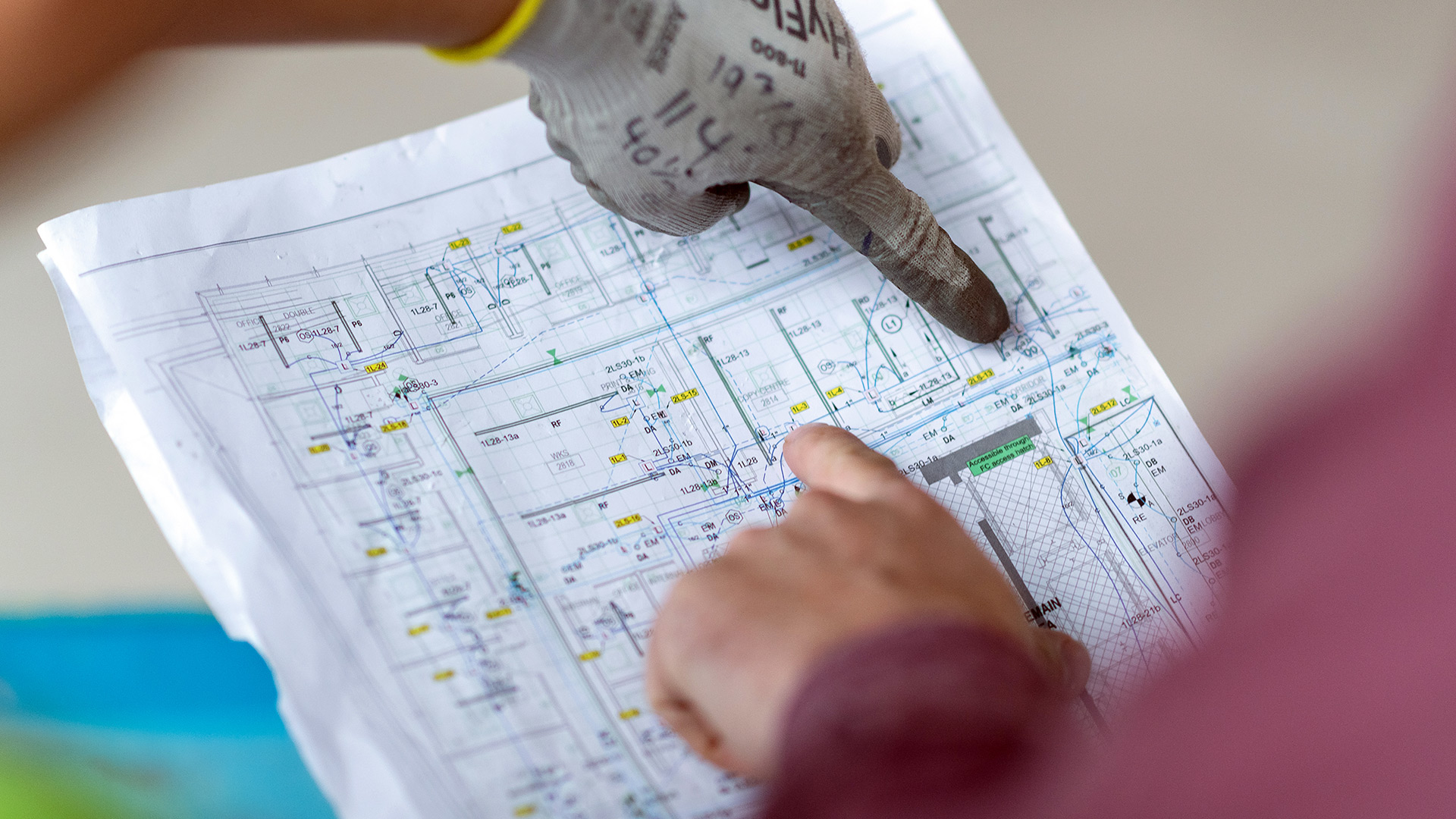 An electrical drawing on some paper with two hands pointing to it.