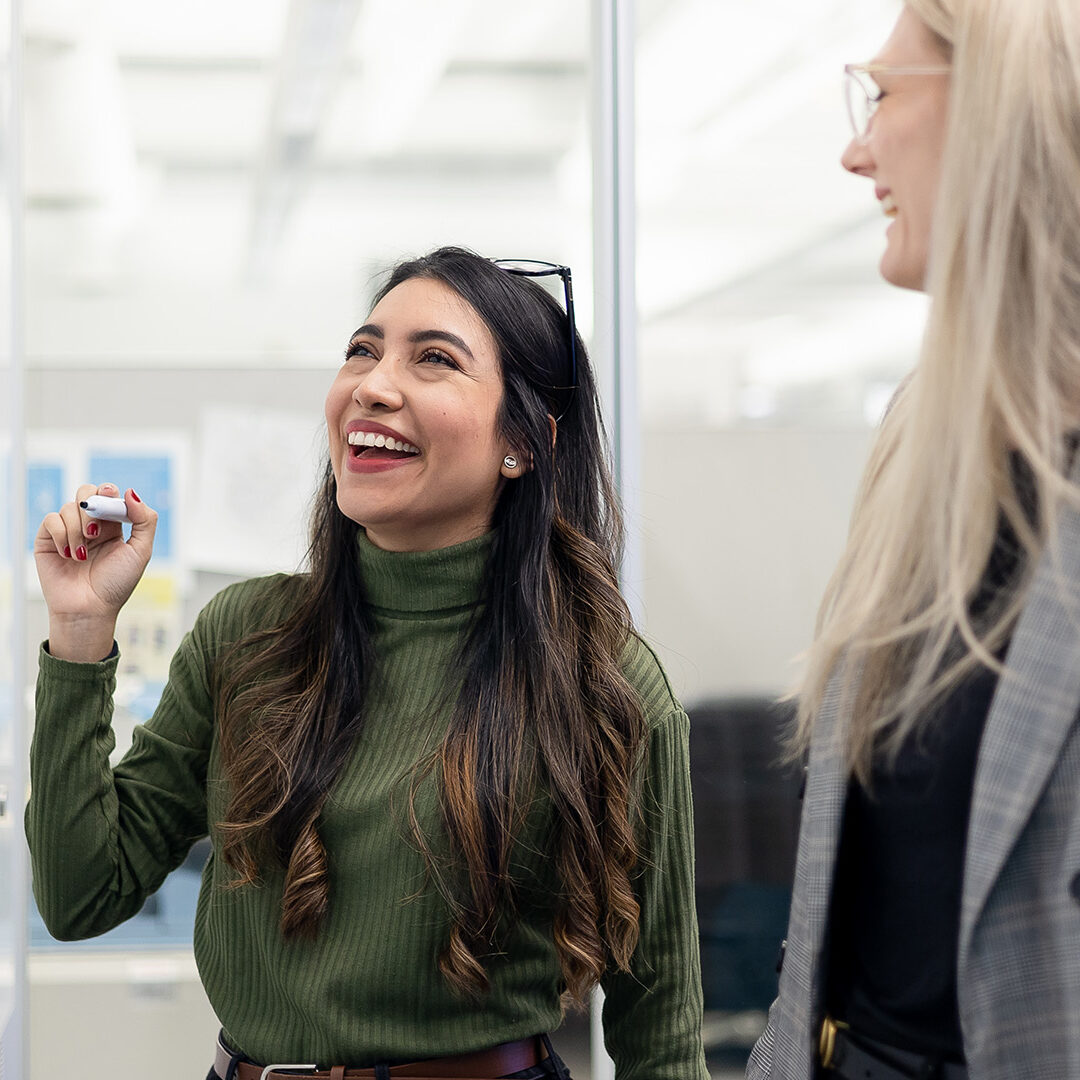 Two people from the Houle team smiling and speaking in front of a whiteboard.