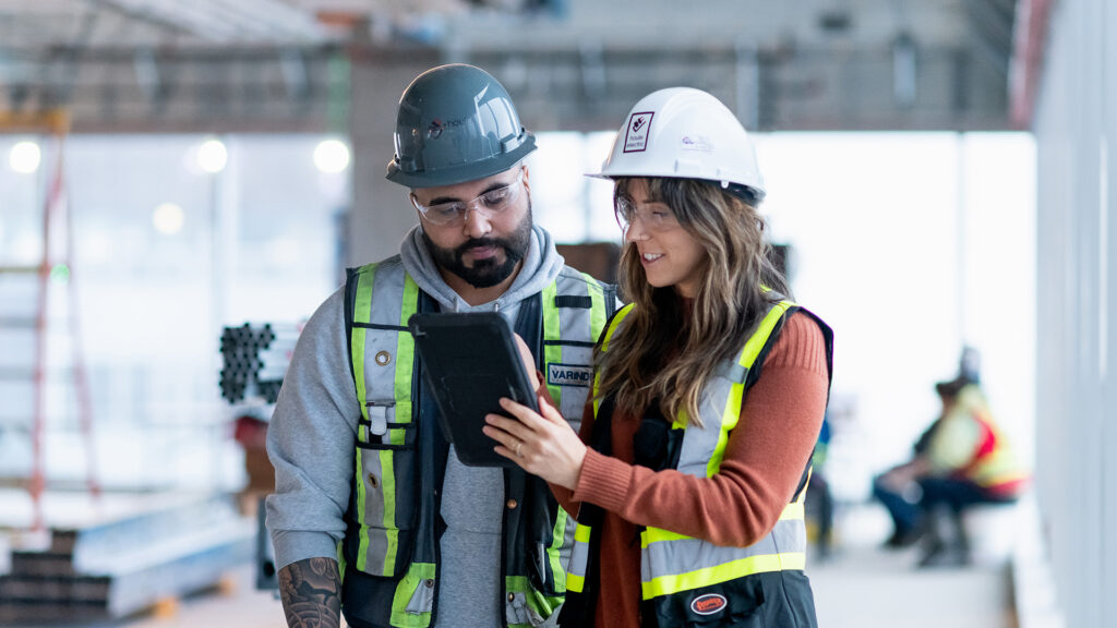 Two Houle employees chatting on site while reviewing drawings on an tablet device